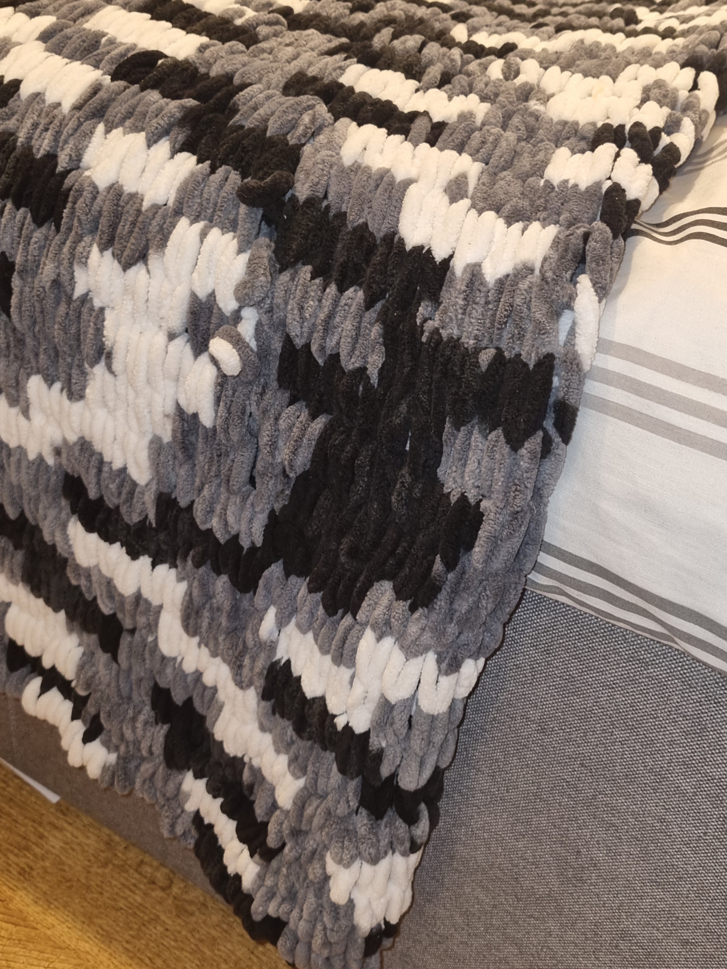 A close-up of a textured throw pillow with a gray, black, and white geometric pattern, resting on a gray sofa next to a striped pillow.